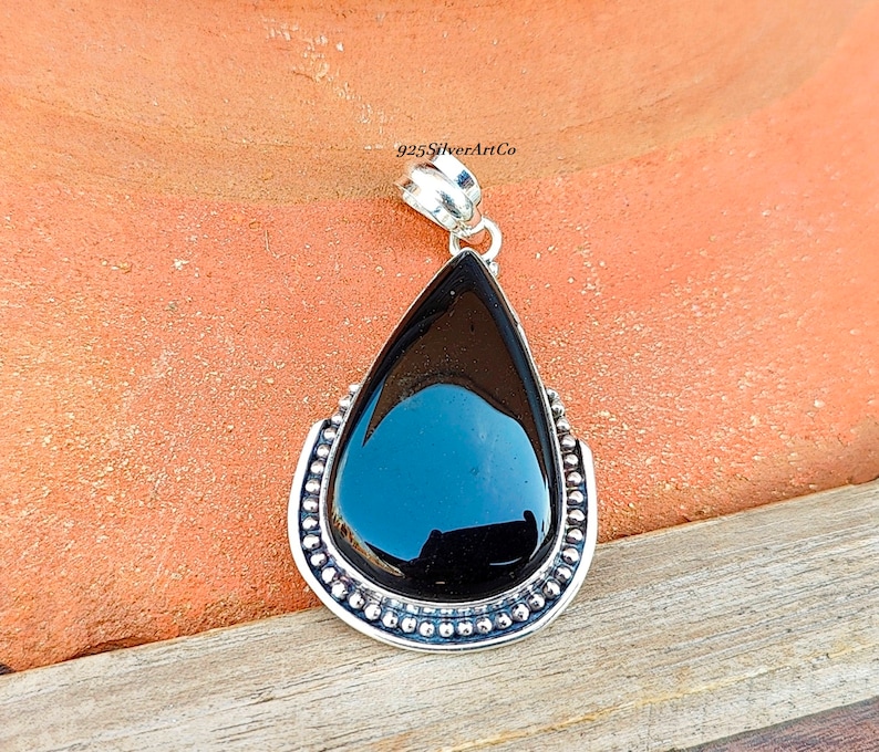 May include: A black onyx pendant with a silver teardrop setting and a beaded border. 925SilverArtCo is printed on the bail.