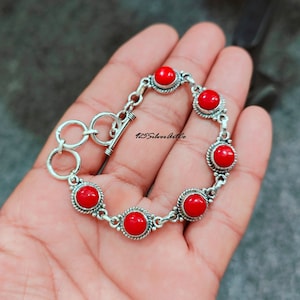 May include: A silver bracelet with six red coral stones. The bracelet has a toggle clasp.
