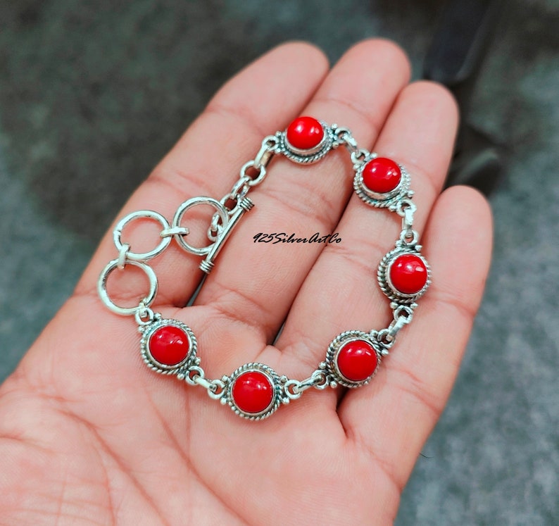 May include: A silver bracelet with six red coral stones. The bracelet has a toggle clasp.