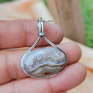 May include: A silver pendant with a white, brown, and gray agate stone. The stone has a banded pattern.