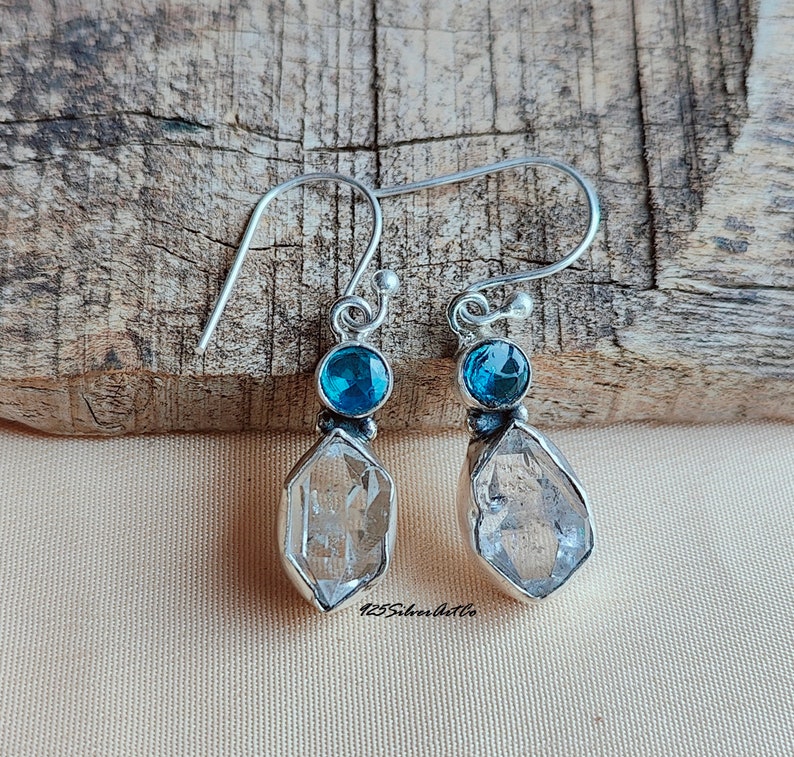 May include: A pair of silver earrings with a clear quartz crystal and a blue gemstone. The earrings have a simple design and are perfect for everyday wear.