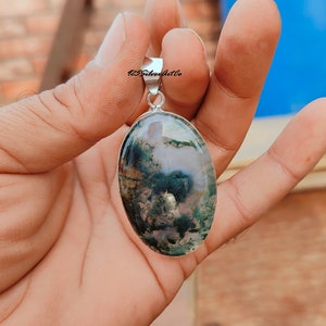 May include: A silver pendant with a green and white moss agate stone. The stone is oval shaped and has a natural, organic pattern.
