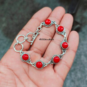 May include: A silver bracelet with six red coral stones. The bracelet has a toggle clasp.
