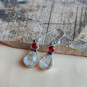 May include: A pair of silver earrings with clear faceted stones and red gemstone accents.