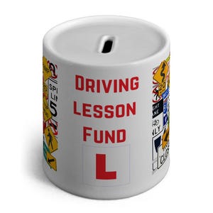 May include: White ceramic money box with a red 'L' on the front and the words 'Driving Lesson Fund' in red. The money box is decorated with various road signs.