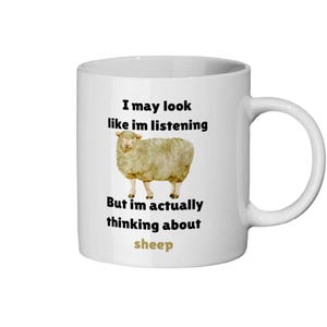 May include: White ceramic mug with a black and white illustration of a sheep and the text "I may look like I'm listening but I'm actually thinking about sheep".