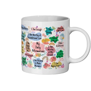 Puede incluir: Taza de cerámica blanca con afirmaciones coloridas como "Soy suficiente" y "Soy digno de mis sueños". La taza tiene un asa curva y está decorada con diseños florales y de arcoíris.