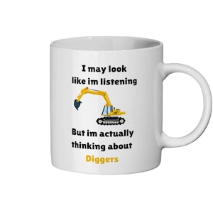 Könnte beinhalten: Eine weiße Keramiktasse mit einer Illustration eines schwarzen und gelben Baggers und dem Text "Ich mag aussehen, als würde ich zuhören, aber eigentlich denke ich über Bagger nach".