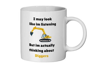 Pode incluir: Caneca de cerâmica branca com uma ilustração de uma escavadeira preta e amarela e o texto "Posso parecer que estou ouvindo, mas na verdade estou pensando em escavadeiras".