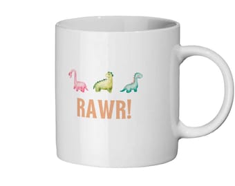 Op de afbeelding: Witte keramische mok met een ontwerp van drie cartoon-dinosaurussen in roze, groen en blauw. De tekst "RAWR!" is in oranje onder de dinosaurussen gedrukt.