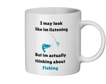May include: White ceramic mug with a black and blue design. The mug features the text "I may look like I'm listening but I'm actually thinking about Fishing" with a blue fish and fishing rod graphic.
