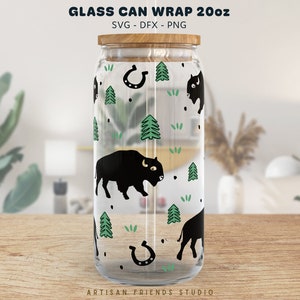 May include: A clear glass can wrap with a wooden lid, featuring a black bison, green trees, and horseshoe pattern. The text "GLASS CAN WRAP 20oz" is at the top. The bottom of the glass has the text "ARTISAN FRIENDS STUDIO".
