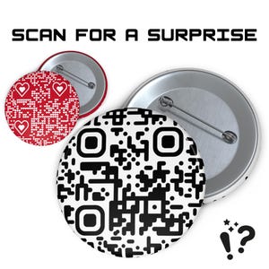 Könnte beinhalten: Drei runde Ansteckbuttons. Einer zeigt einen QR-Code, ein anderer ein rot-weißes Muster mit Herzen und der dritte eine silberne Rückseite. Der Text "SCAN FOR A SURPRISE" steht über den Buttons.