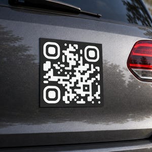 Puede incluir: Una pegatina cuadrada con un código QR en blanco y negro aplicada en la parte trasera de un vehículo gris oscuro. El diseño presenta un patrón de alto contraste de cuadrados blancos sobre un fondo negro sólido, centrado en la superficie.