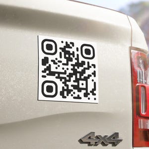 Könnte beinhalten: Ein quadratischer weißer Aufkleber mit einem schwarzen QR-Code-Muster. Der Aufkleber ist auf der hellen Heckklappe eines Fahrzeugs angebracht, links vom roten Rücklicht und oberhalb des silbernen 4x4-Emblems im unteren Bereich der Heckklappe.
