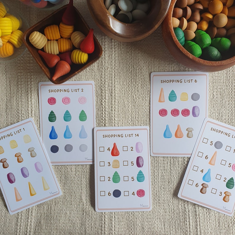 May include: Five colorful cards with shopping lists for a game. The lists include numbers, squares, and circles with different colored shapes inside. The cards are on a beige surface.