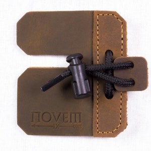 May include: Brown leather archery finger tab with a black adjustable strap and the word "POVEII" embossed on the leather.