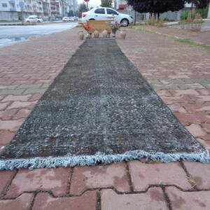 May include: A long, dark gray runner rug with a light blue fringe. The rug is laid out on a brick walkway.