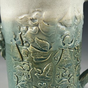 May include: A ceramic mug with a green and white glaze. The mug has a raised design of angels and doves.