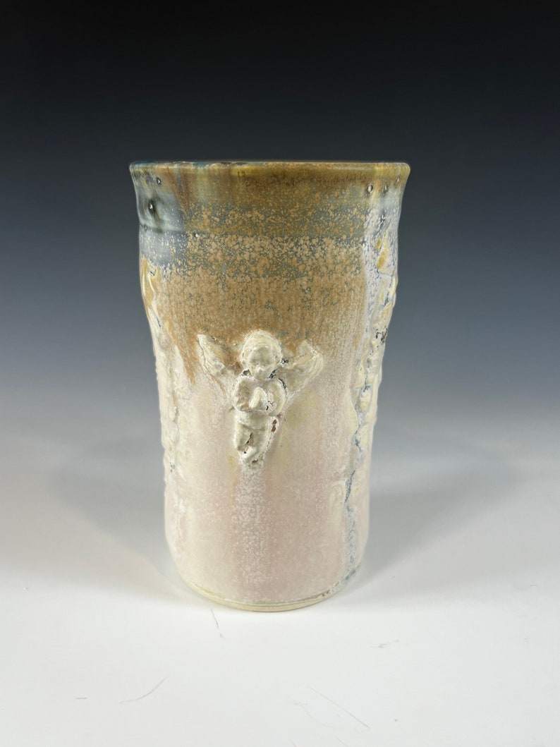 May include: A ceramic vase with a light brown, white, and blue glaze. The vase has a textured surface with raised designs of angels.