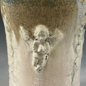May include: A ceramic vase with a textured, speckled glaze in shades of brown, gray, and white. The vase features a raised, sculpted angel design.