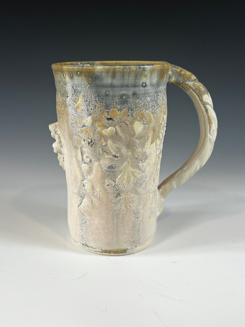 May include: A white ceramic mug with a textured, floral design and a brown handle. The mug has a speckled glaze and a slightly uneven surface.
