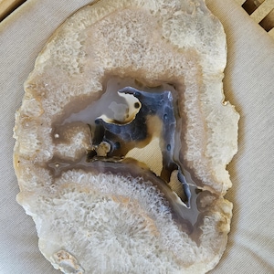 May include: A large, white agate slice with a brown and gray center. The agate has a natural, organic shape and a smooth, polished surface.