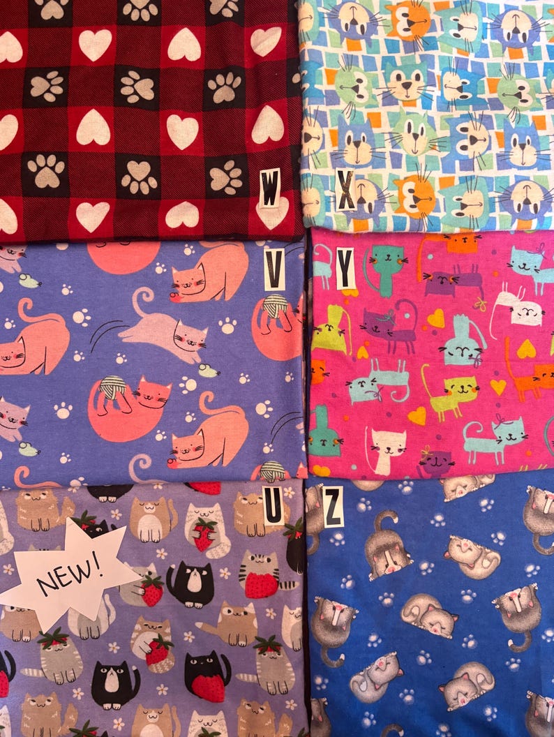 May include: Six fabric swatches featuring various cat-themed patterns. Top left is red and black buffalo plaid with white hearts and paw prints labeled W. Top right is a blue and white grid with cat faces labeled X. Middle left is purple with pink cats labeled V. Middle right is pink with colorful cats labeled Y. Bottom left is light purple with cats holding strawberries labeled U and NEW. Bottom right is blue with sleeping cats labeled Z.