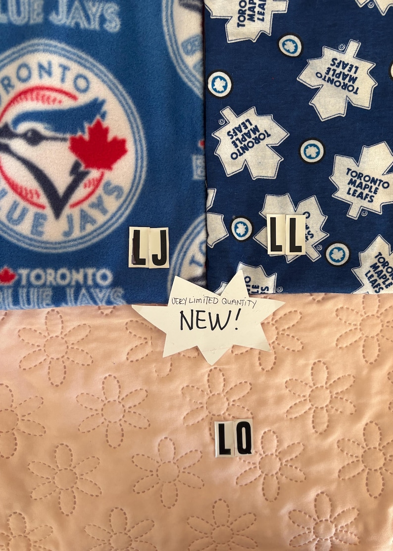 May include: Two pieces of fabric featuring sports team logos. The left fabric is blue with the Toronto Blue Jays logo. The right fabric is dark blue with the Toronto Maple Leafs logo. A white star-shaped sign reads "VERY LIMITED QUANTITY NEW!"