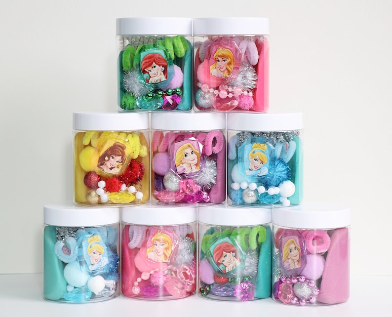 May include: Eight clear plastic jars with white lids filled with various colorful craft supplies, including pom poms, beads, and glitter. Each jar features a different Disney princess character sticker.