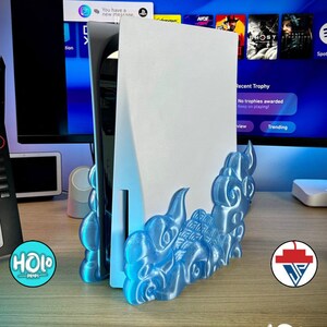 Puede incluir: Un soporte de impresión 3D azul para una consola Playstation 5. El soporte tiene forma de llama estilizada y tiene un acabado brillante.