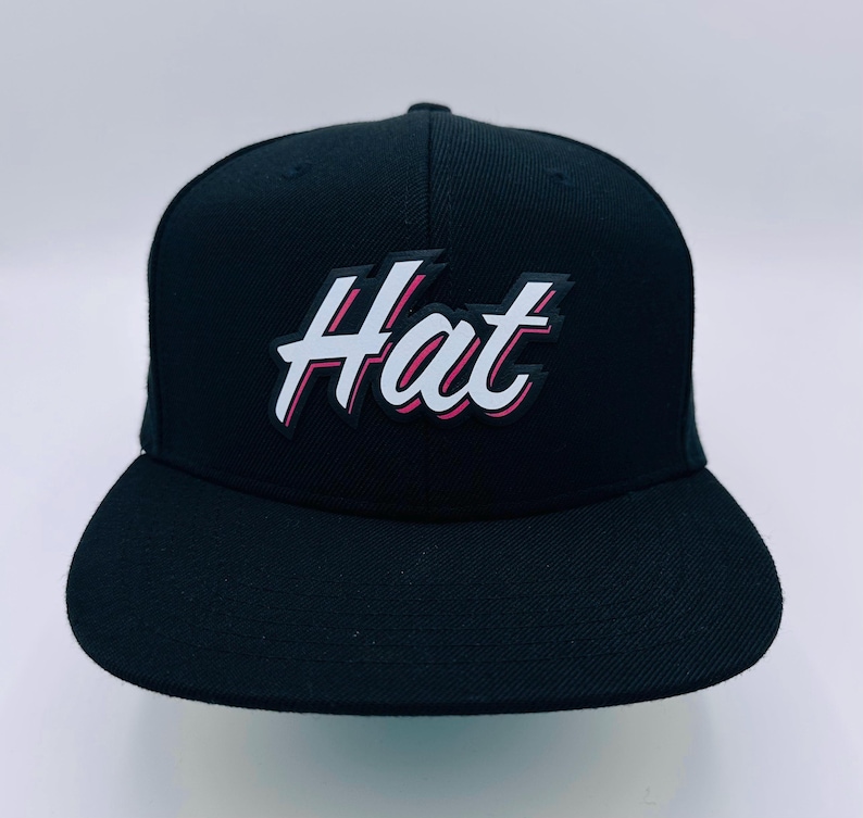 Puede incluir: Una gorra de b&eacute;isbol negra con un logotipo blanco "Hat" en un contorno rosa y blanco.