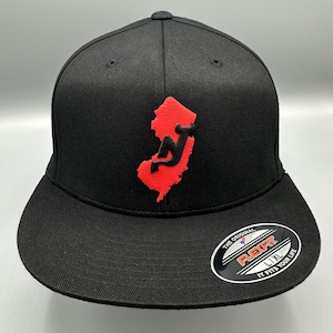 May include: Black baseball cap with a red and black New Jersey state outline logo. The cap has a Flexfit label on the back.