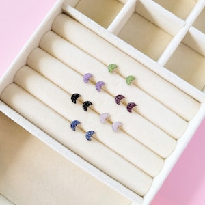 May include: A set of 10 crescent moon shaped earrings with various coloured crystals. The earrings are displayed in a white box with multiple compartments.
