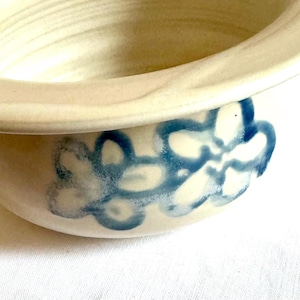 May include: A white ceramic bowl with a blue floral design. The bowl has a wide rim and a rounded bottom.