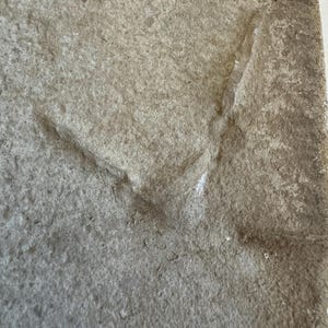 May include: Close-up of a rough, gray, textured surface with a crack running diagonally across it.