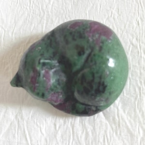 May include: A green and pink gemstone carved into the shape of a sleeping cat. The gemstone has a smooth, polished surface.