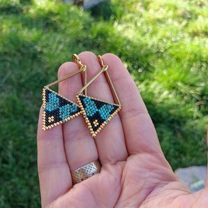 Puede incluir: Un par de pendientes triangulares de oro con diseños de cuentas negras y turquesa.