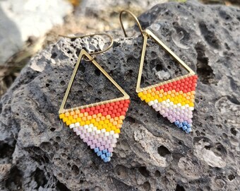 May include: A pair of handmade earrings featuring a geometric triangle design. The earrings have a gold-colored metal frame and are filled with colorful beads in a gradient pattern of red, orange, yellow, white, pink, and blue.