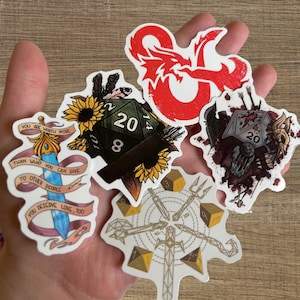 Puede incluir: Cinco pegatinas con un dragón rojo, un dado de 20 caras, una espada, una calavera y una brújula. Las pegatinas tienen un fondo blanco y contornos negros. El texto en las pegatinas dice "You are worth more than what you can give to other people. You deserve love too."