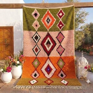 May include: A rectangular area rug featuring three horizontal colour blocks in olive green, soft pink, and bright orange. The rug is decorated with a repeating diamond pattern in contrasting colours including red, white, black, and purple, finished with a fringe.