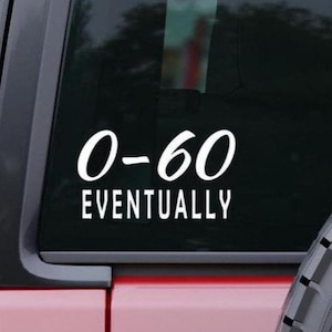 May include: White vinyl decal with the text "0-60 EVENTUALLY" on a vehicle window. The decal is in a sans-serif font. The vehicle is red with a black window and a tire visible on the right side.