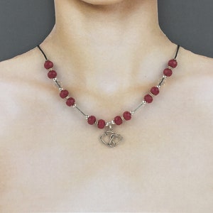 Op de afbeelding: Een rode kralenketting met een zilveren dubbele hartbedel. De ketting is gemaakt met gefacete rode kralen en zilveren tussenkralen.