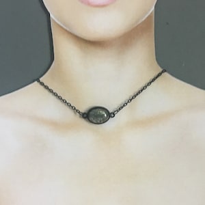 May include: A delicate black chain necklace with a small oval-shaped pendant featuring a green and black speckled stone.