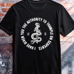 May include: A black short-sleeve t-shirt featuring a white circular graphic. The design depicts a sword entwined with a snake, surrounded by the text I HAVE GIVEN YOU THE AUTHORITY TO TRAMPLE ON SERPENTS, with LUKE 10 19 printed on the sides.