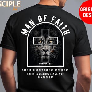 May include: Black t-shirt with a white graphic featuring a lion's face within a cross, the words "MAN OF FAITH" and "DISCIPLE" are above the lion. Below the lion is the text "1 TIMOTHY 6:11" and a quote about righteousness.