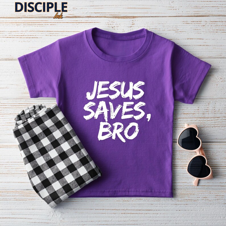 Op de afbeelding: Een paars T-shirt met de tekst "JESUS SAVES, BRO" in het wit. Daarnaast een zwart-wit geruite broek en een hartvormige zonnebril.