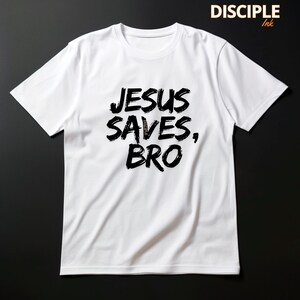 Op de afbeelding: Wit T-shirt met de tekst "JESUS SAVES, BRO" in vette, zwarte letters. Het shirt heeft ook de tekst "DISCIPLE Ink" in de rechterbovenhoek. Het shirt is gemaakt van een zacht, comfortabel materiaal.