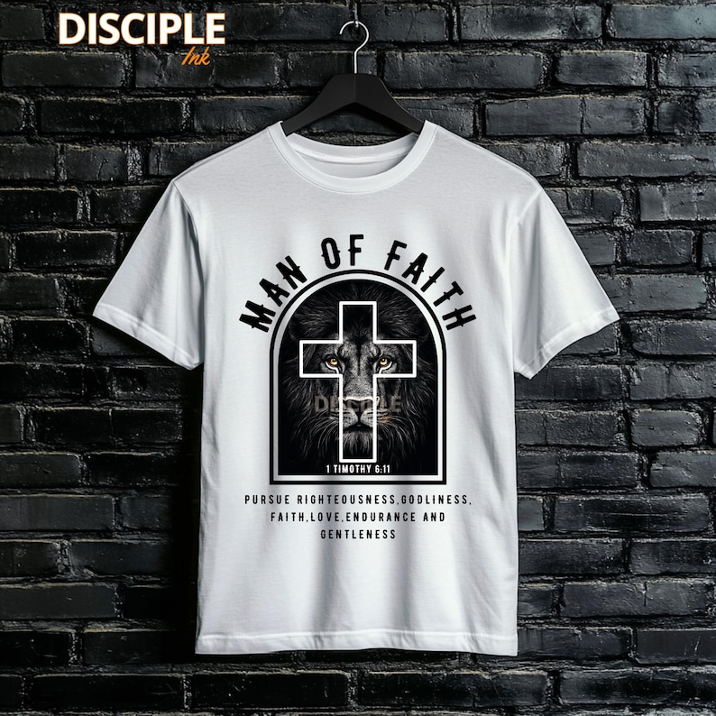 May include: White t-shirt with a black graphic featuring a lion's face within a cross, and the words "MAN OF FAITH." The text "1 Timothy 6:11" and a list of virtues are printed below the graphic. The brand "DISCIPLE Ink" is at the top.