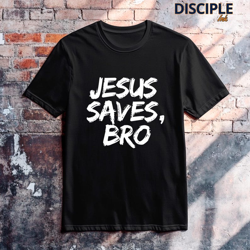 Op de afbeelding: Zwart T-shirt met de witte tekst "JESUS SAVES, BRO" in een gedurfde, handgeschreven stijl. Het shirt heeft een ronde hals en lijkt gemaakt van een zacht materiaal. De merknaam "DISCIPLE Ink" staat rechtsboven gedrukt.